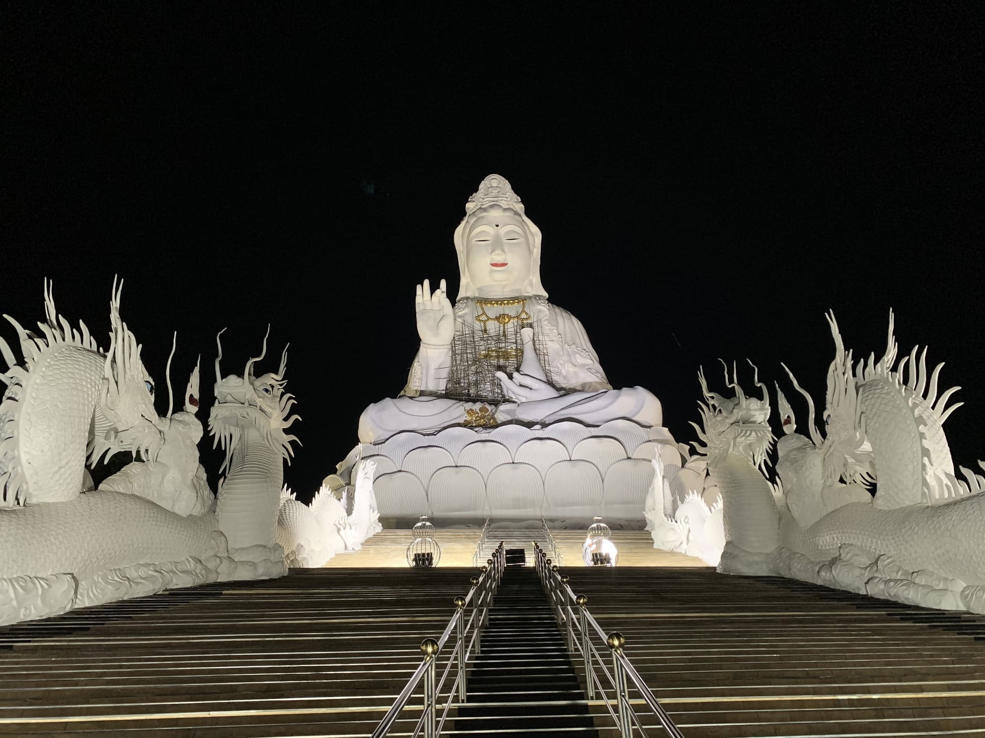 Giant white Guan Yin statue and dragon balustrades of Wat Huay Pla Kang lit at night