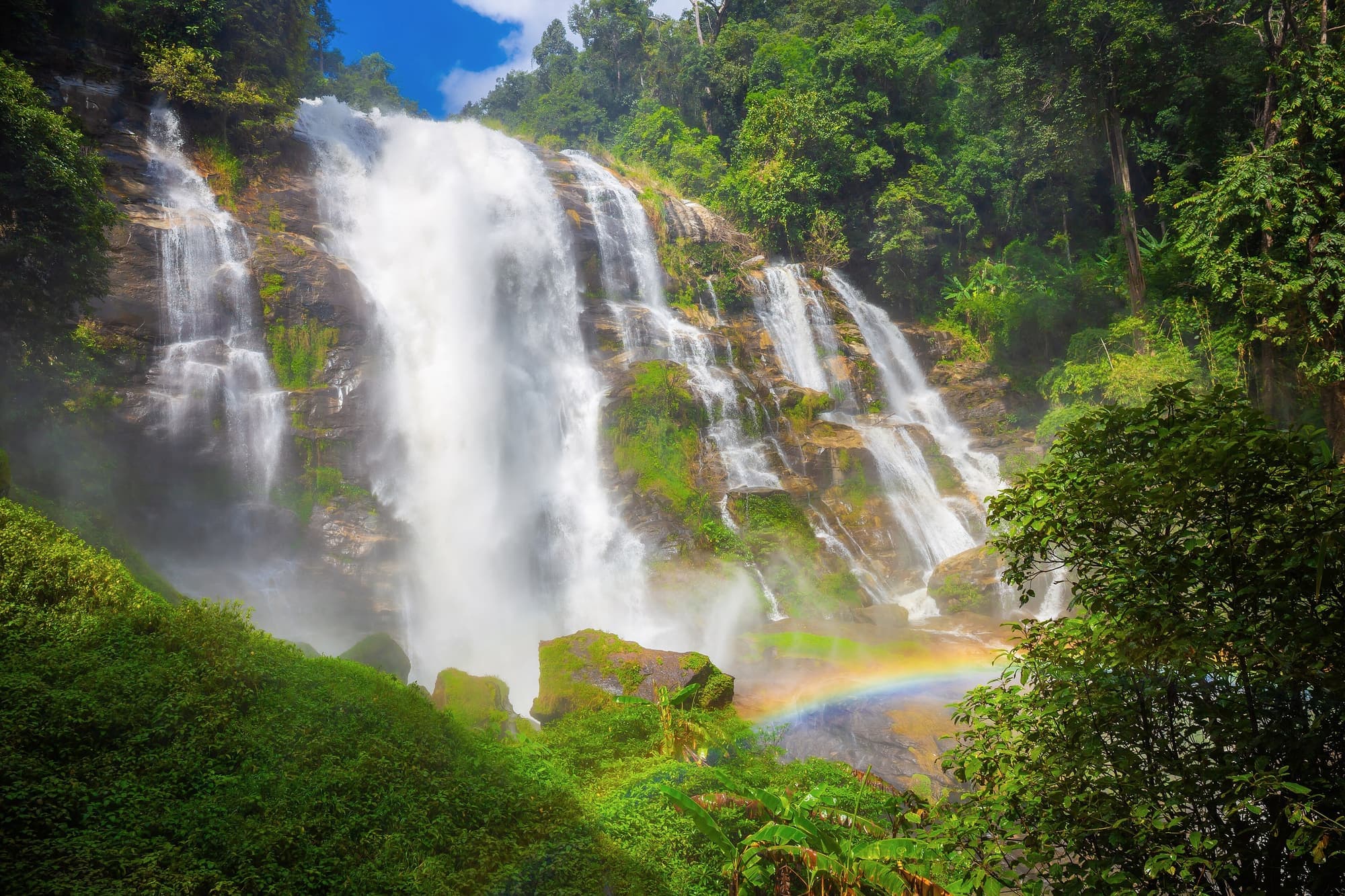 Wachirathan Waterfall thundering down a cliff with a rainbow in its spray
