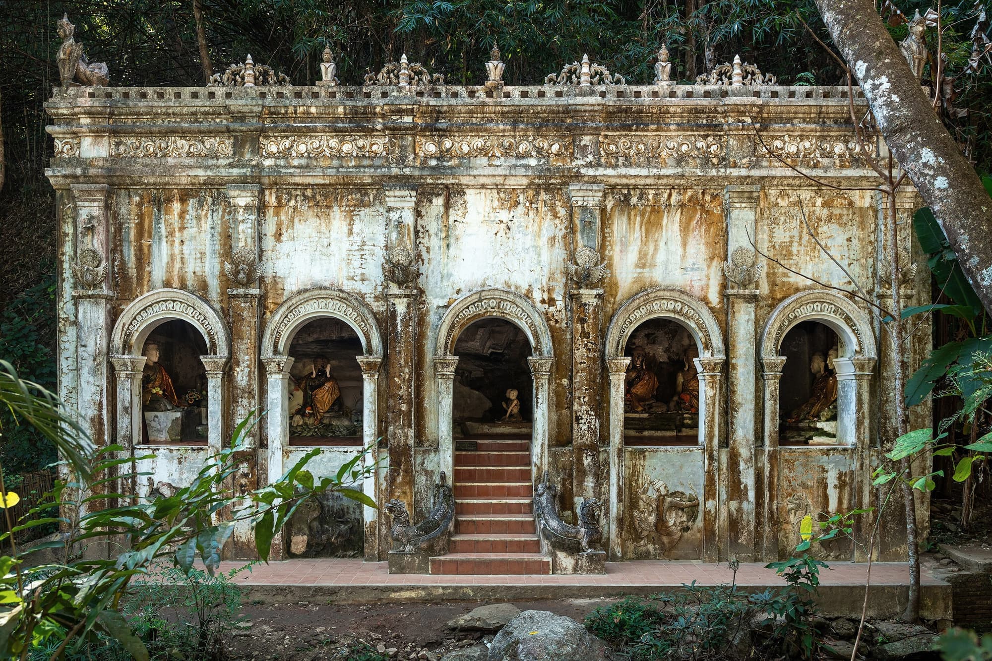 Weathered white hall of Wat Pha Lat surrounded by jungle