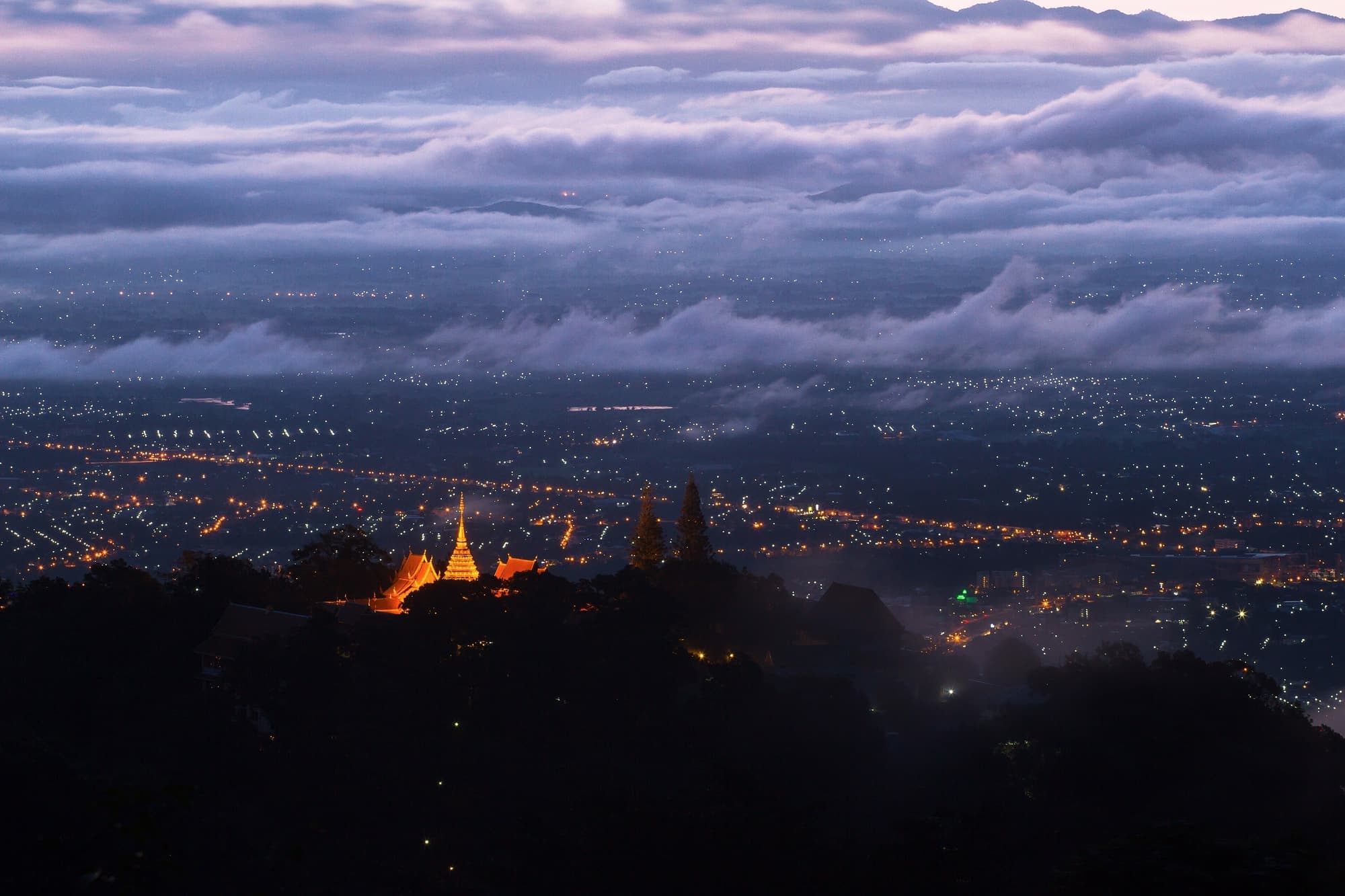 Doi Suthep temple glowing above a sea of cloud and the lights of Chiang Mai at dawn